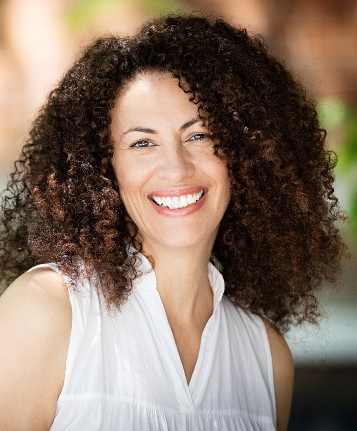 Smiling woman with curly hair in white top.