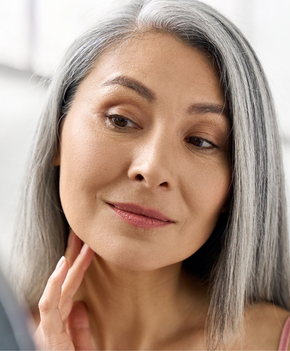 Woman with gray hair examining her skin.